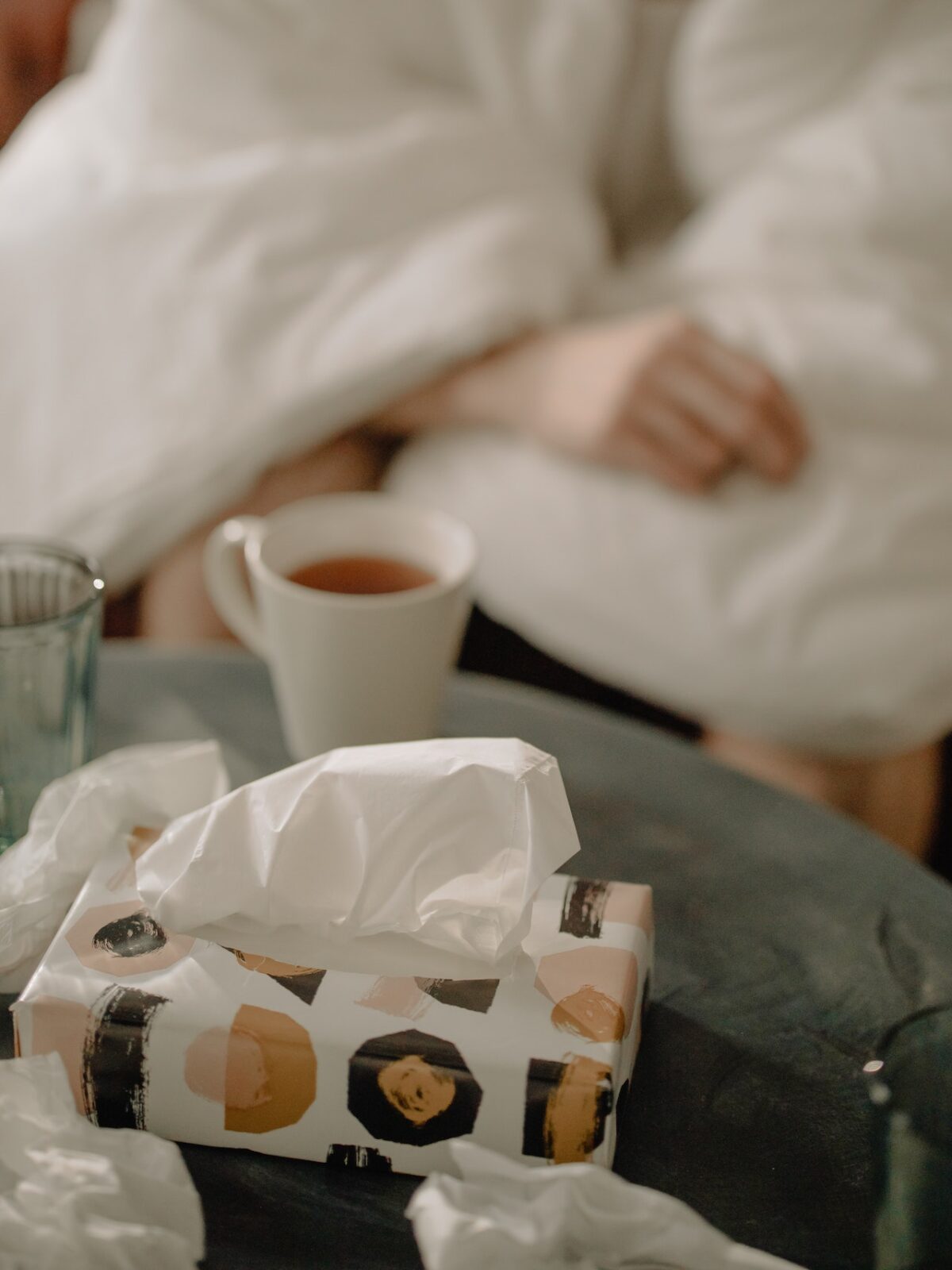 used tissues, hot tea, person wrapped in blanket
